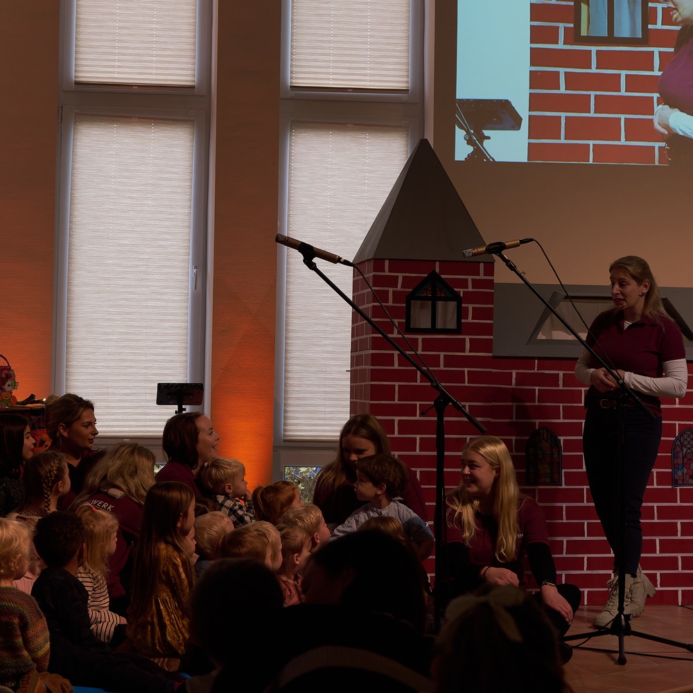 Kinder und Mitarbeiter sitzen vor einer Puppenkirche und hören gespannt zu. 