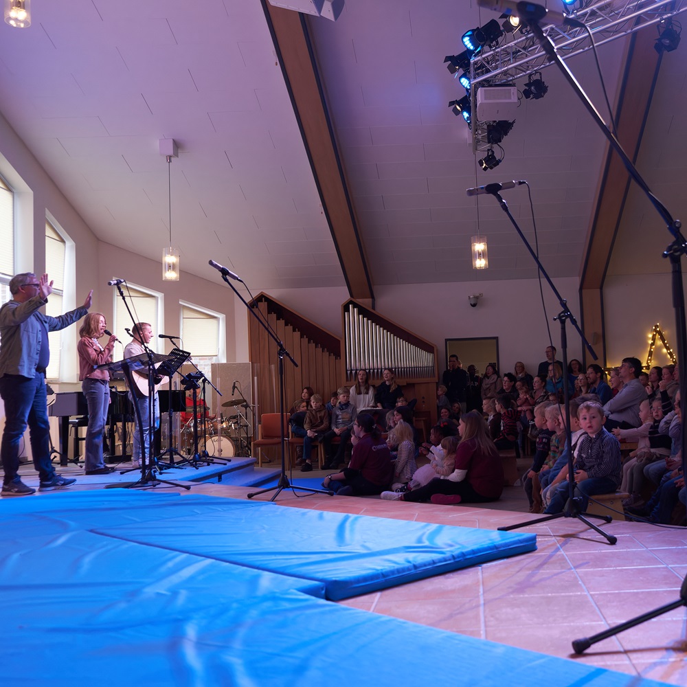 Blick von der Seite auf die Bühne. Der Pastor, die Band und einige Gottesdienstbesucher sind zu sehen. 